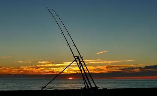 Balık Avı Teknikleri Gün batımında kıyıda kurulmuş surf casting kamış ve makine takımı görseli
